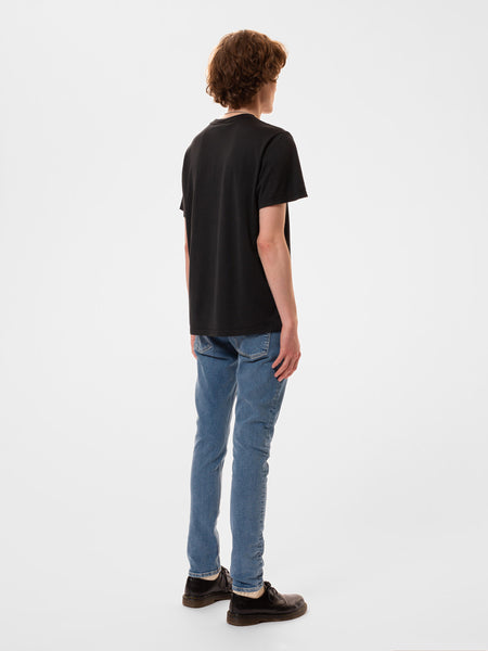 T-Shirt von Nudie Jeans in verwaschenem Schwarz, Print auf der Vorderseite "No Shock No Progress". Ansicht von hinten, das Shirt hat keinen Print auf der Rückseite.