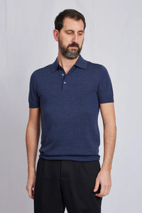 Ein männliches Model trägt das Poloshirt in Kombination mit einer schwarzen, locker geschnittenen Chino.