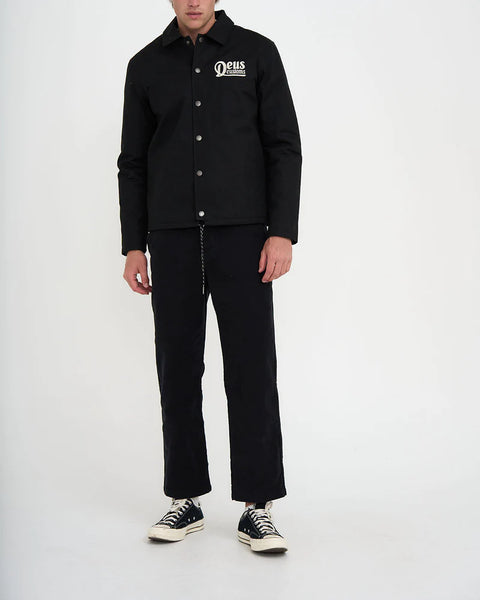 Ein männliches Model trägt die Hose mit einer schwarzen Jeans und schwarzen Chucks.