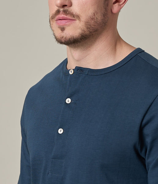Merz b. Schwanen Henley in Langarm in der Farbe Mineral Blue, ein Mittelblau mit einer leichten Washed-Optik. Detailaufnahme der echten Oerlumtt-Knöpfe an der Knopfleiste.