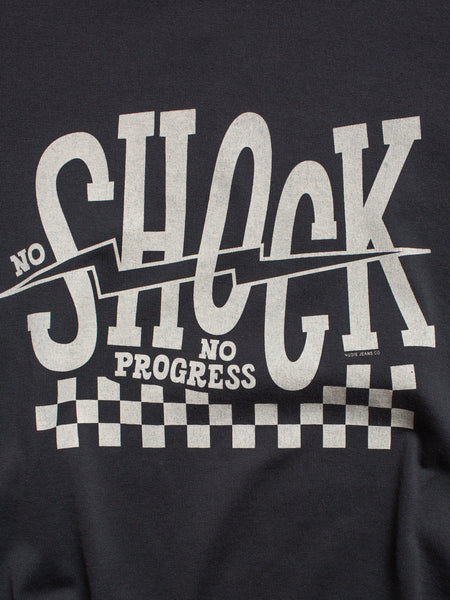 T-Shirt von Nudie Jeans in verwaschenem Schwarz, Print auf der Vorderseite "No Shock No Progress". Detailaufnahme des Prints in Off-White.